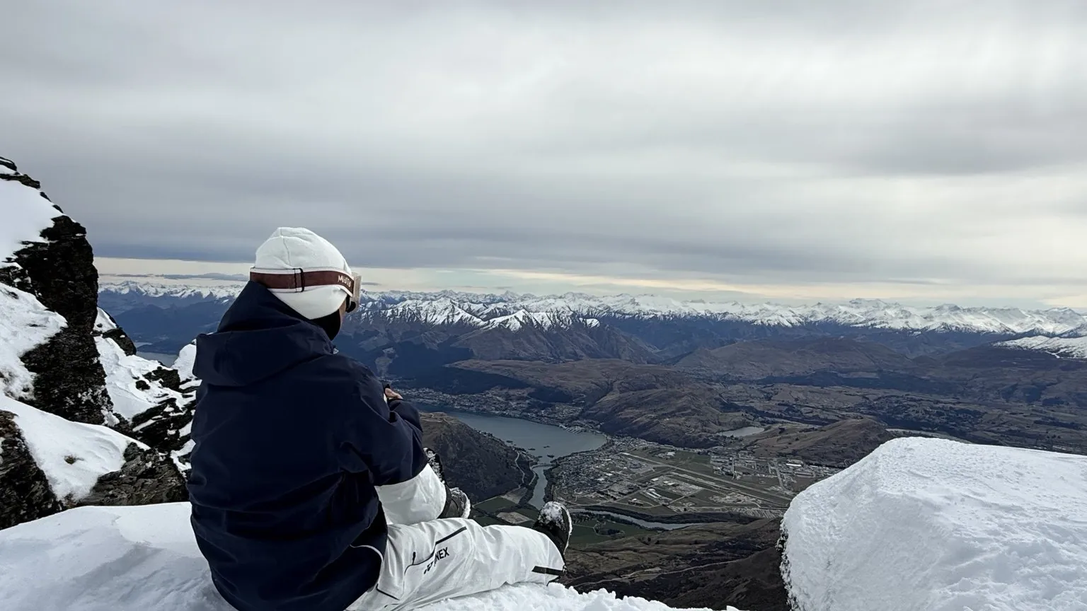 运动员坐在雪坡边望向远处的山谷雪景